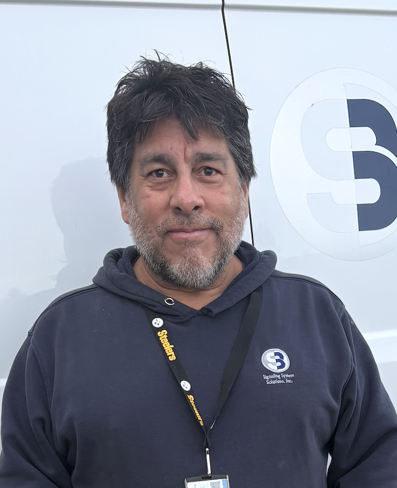 Man wearing a navy hoodie with a logo, standing in front of a white background.