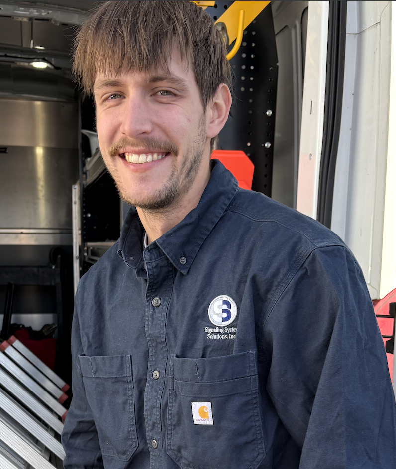 A smiling man in a navy blue uniform stands near a vehicle.
