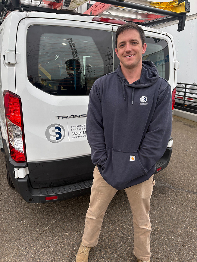 Man smiling, standing next to a white van outdoors.