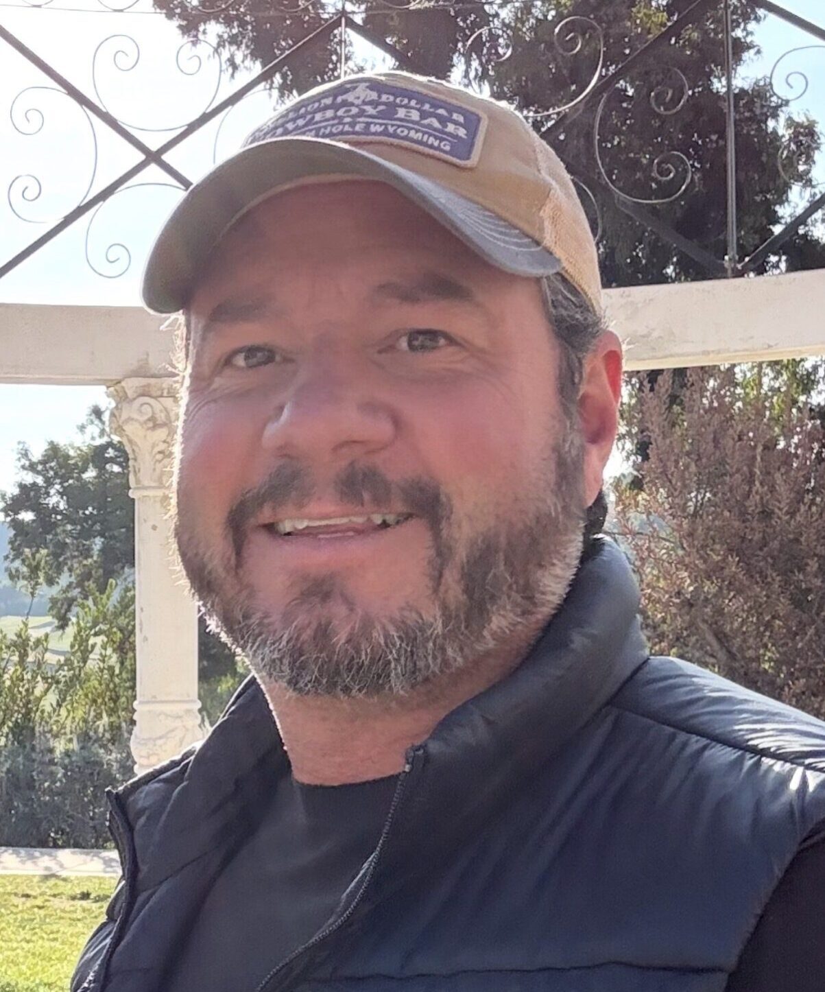 Smiling man wearing a cap and jacket outdoors.