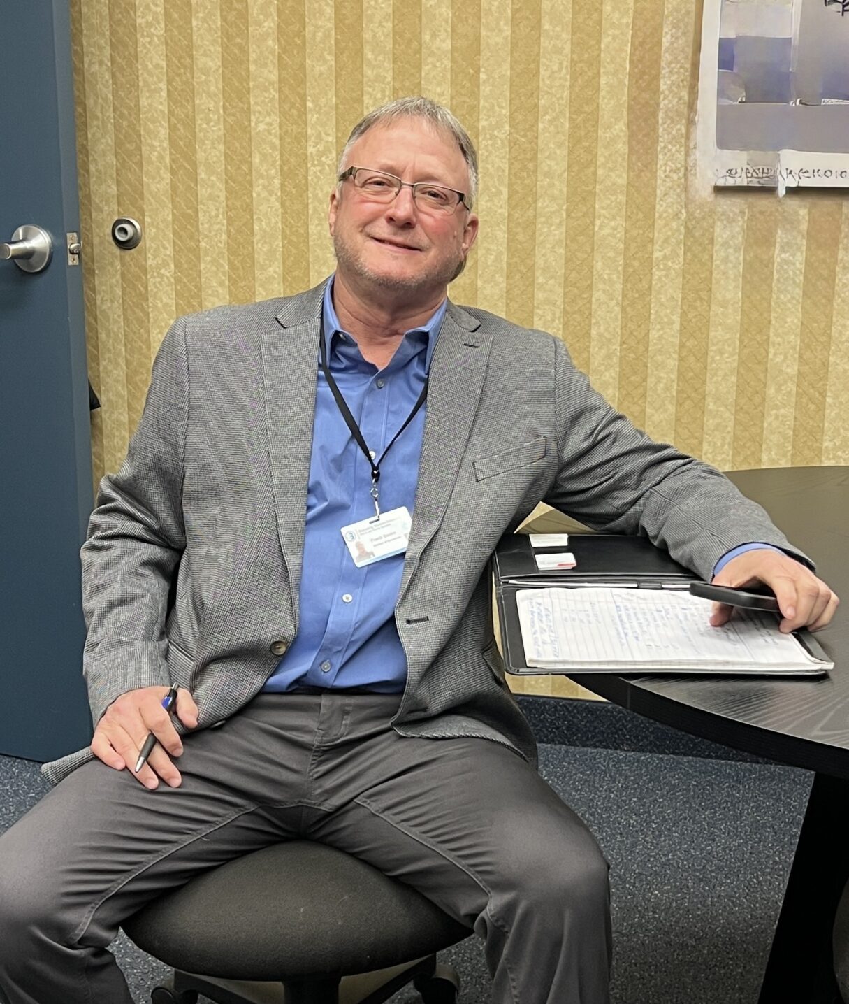 A relaxed man in a gray suit sitting in an office chair.